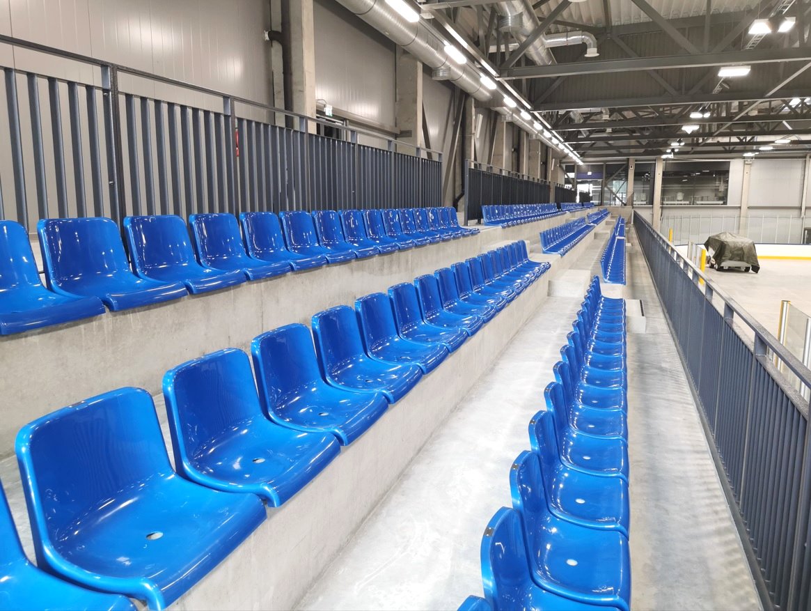 Blue tiered rinkside seating along an indoor ice rink